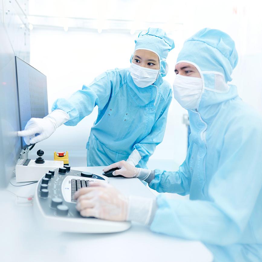 Two employees work on a screen in the clean room and discuss results of their latest research