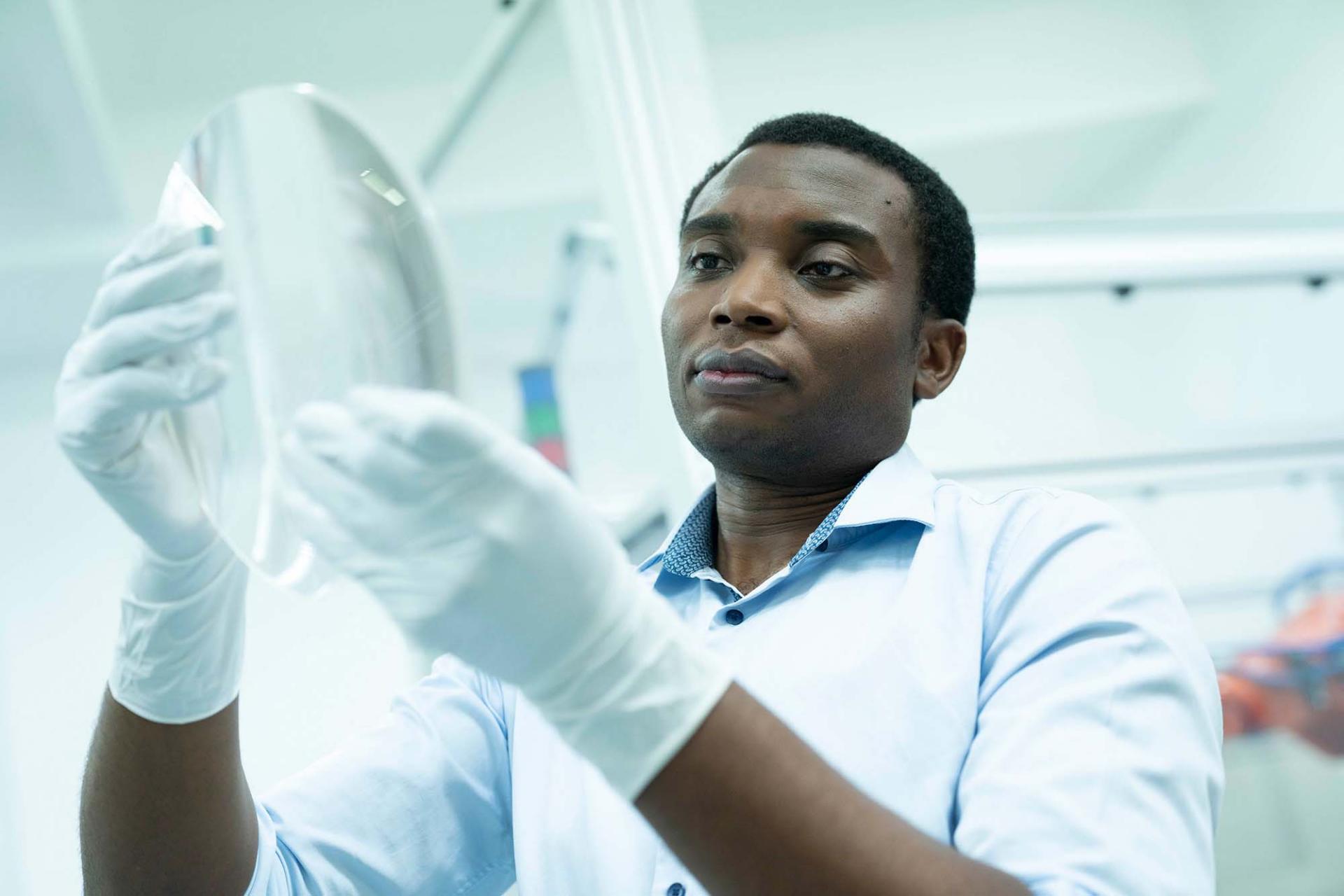 A ZEISS SMT employee holds up a lens and looks at it intently.  