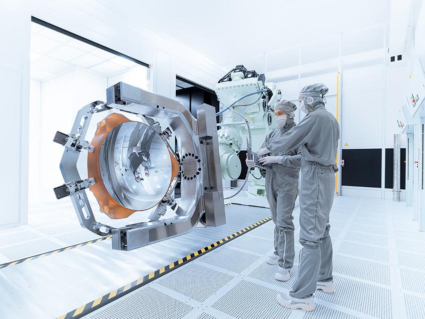 Two employees work on a mirror of the High-NA-EUV technology in the clean room