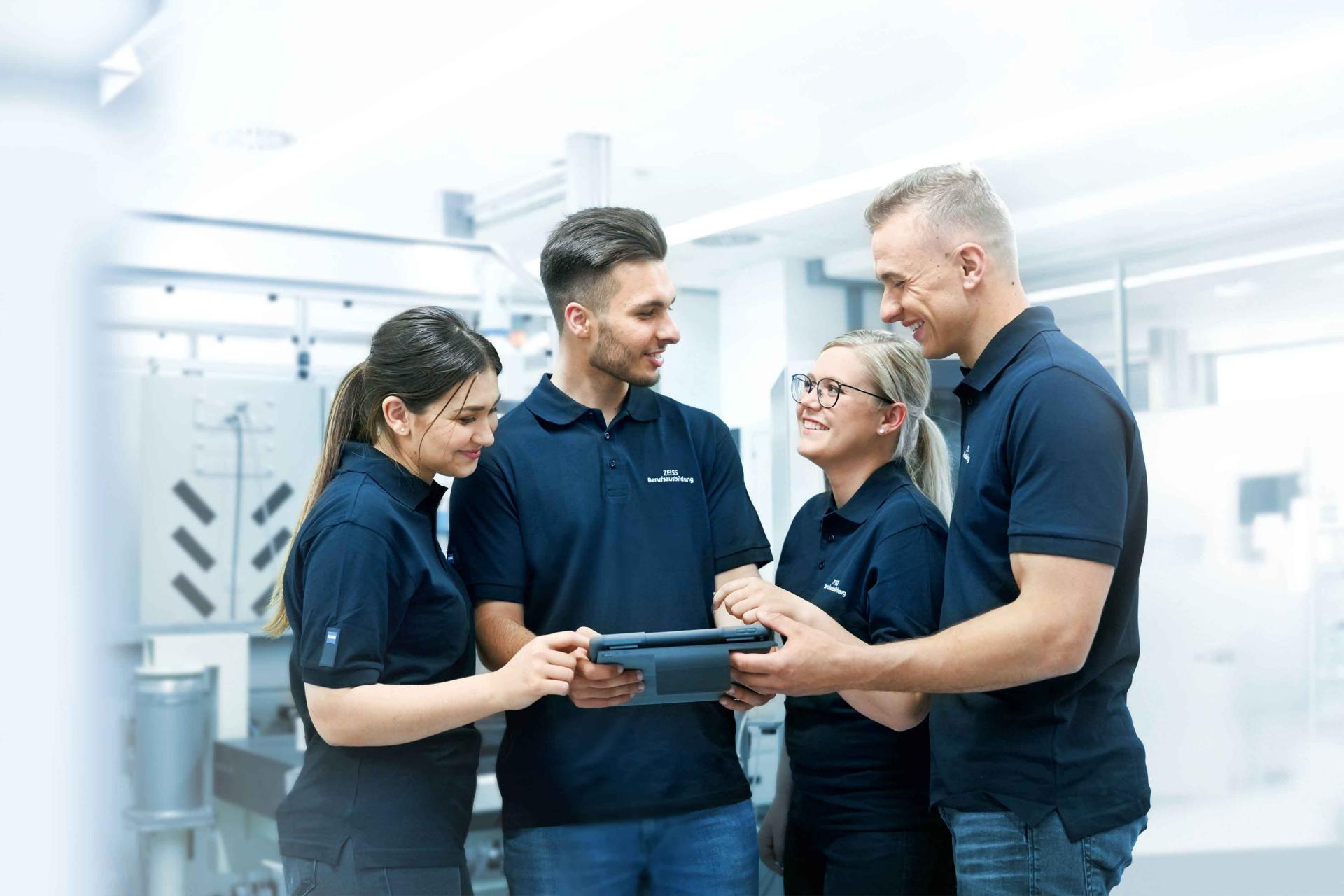 Trainees look together at a tablet in Production at ZEISS SMT