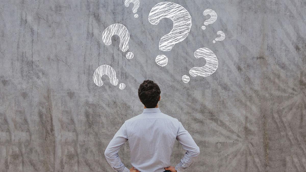 A man stands in front of a gray wall and is surrounded by question marks