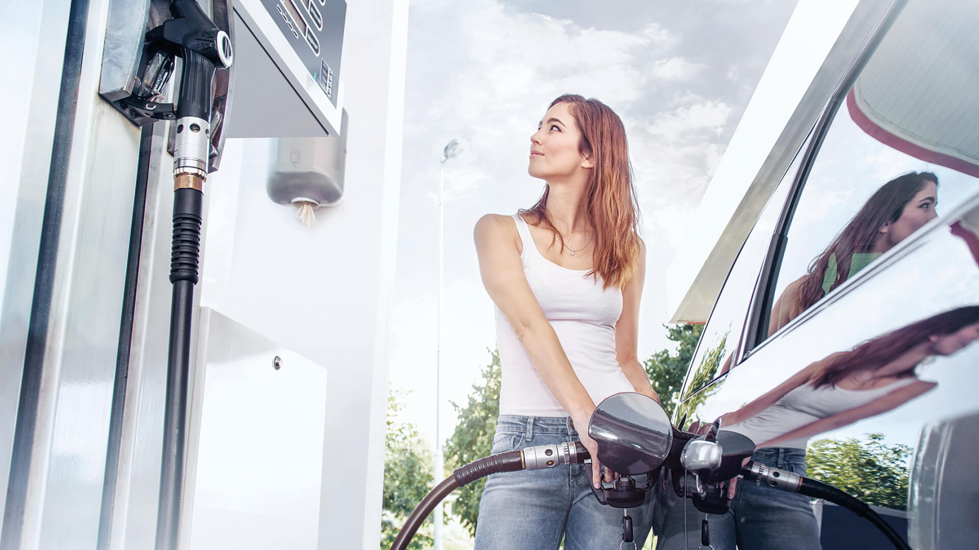 young woman stands at the petrol pump of a gas station and fills her vehicle with corn-based ethanol