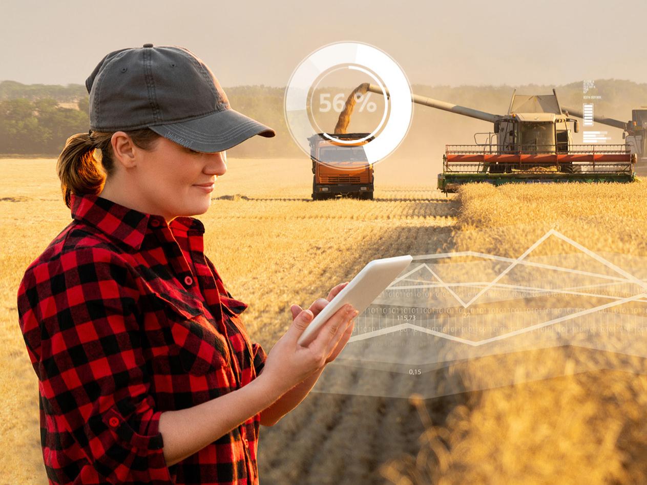 Woman farmer with digital tablet on a background of harvesters