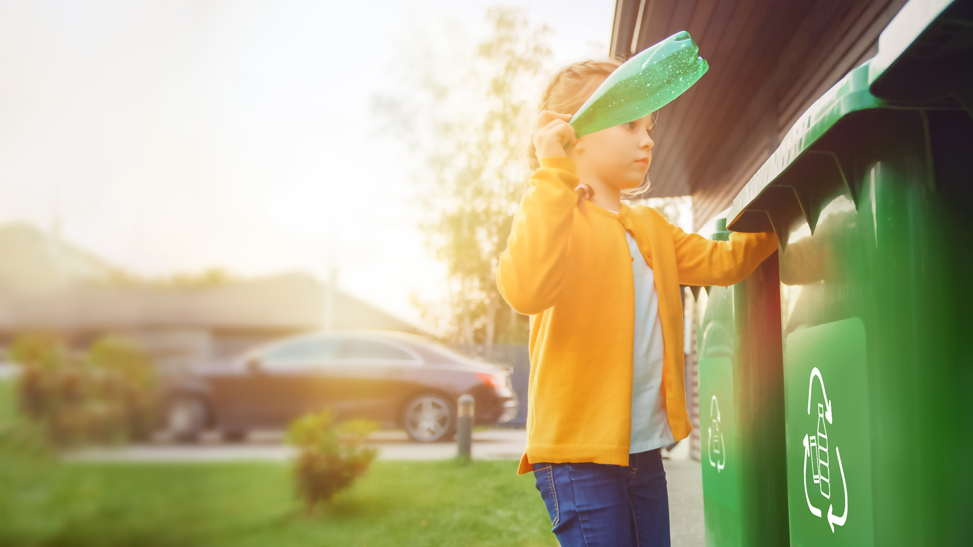 Young girl is throwing away an empty plastic bottle into a trash bin. She uses correct garbage bin. Recycling