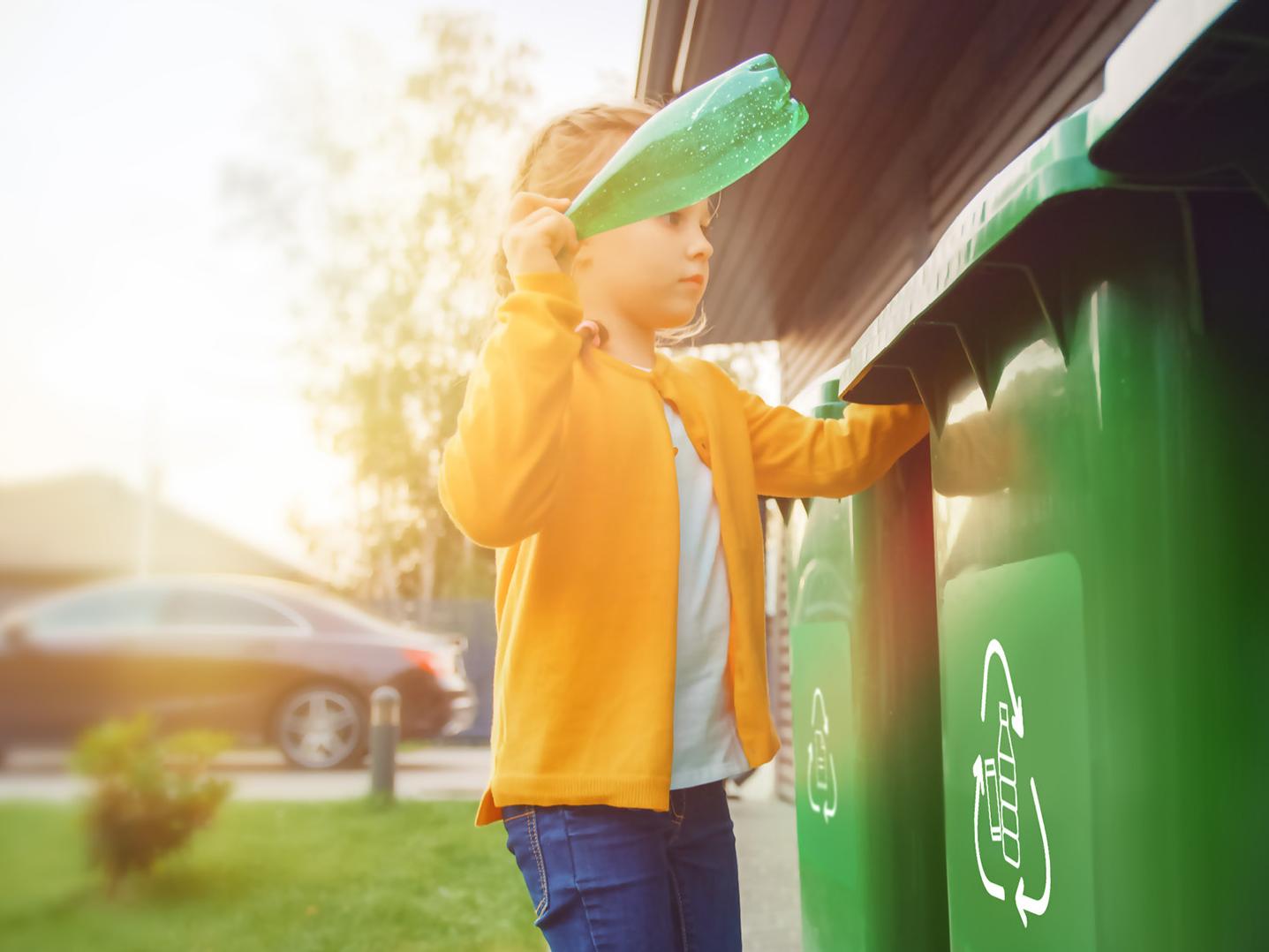 Young girl is throwing away an empty plastic bottle into a trash bin. She uses correct garbage bin. Recycling