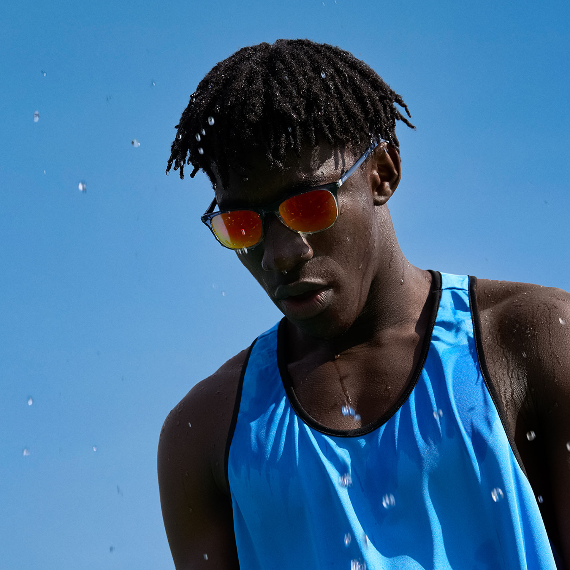 A young man in sportwear and ZEISS Performance sunglass lenses in a brown-orange tone in front of the blue sky.