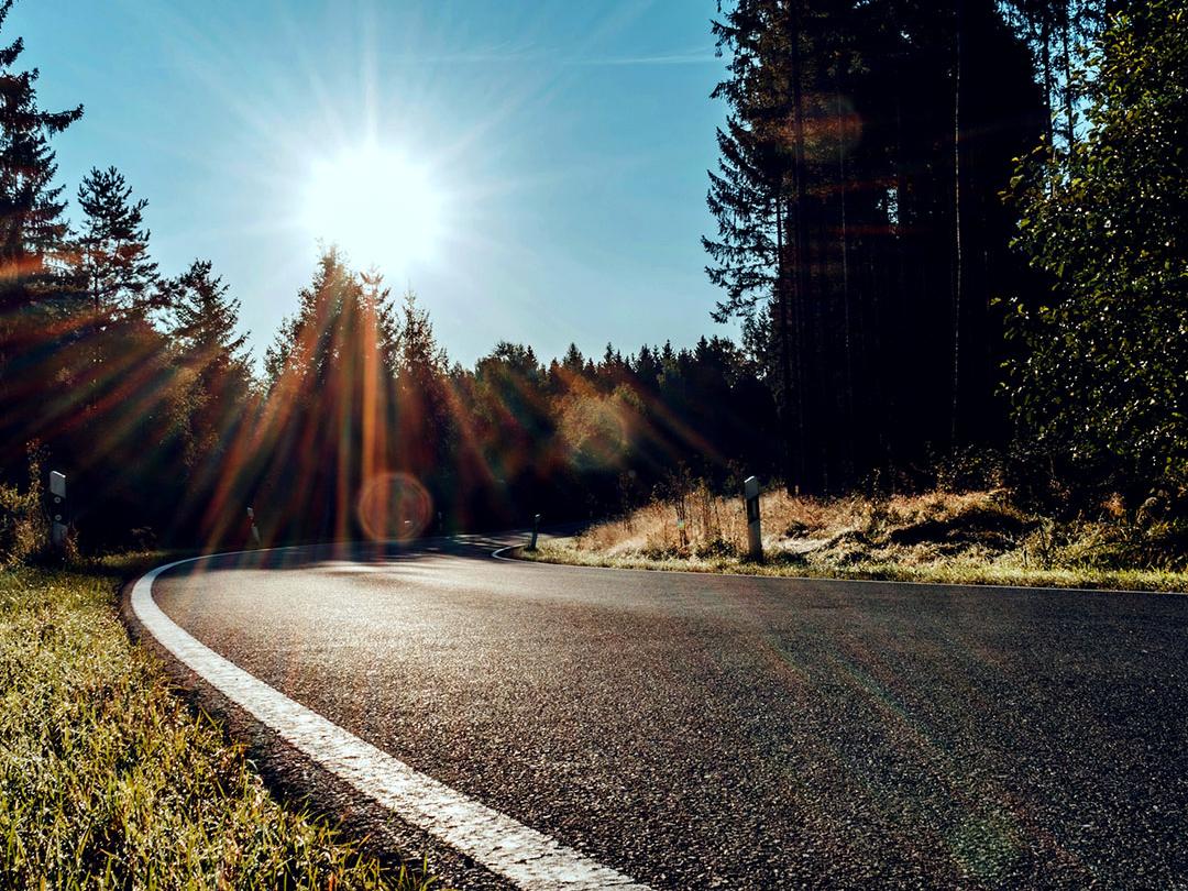 A slider image where one half shows a road in the woods with bright light from a sun, and the other half showing the same road with reduced glare and increased contrast, emphasising the effect of polarized sunglass lenses.