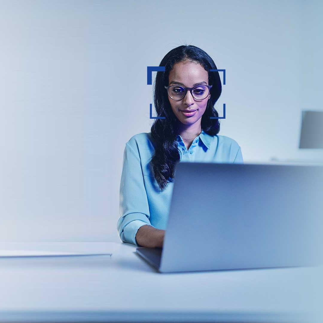 Woman with black hair and glasses watches smiling into a laptop