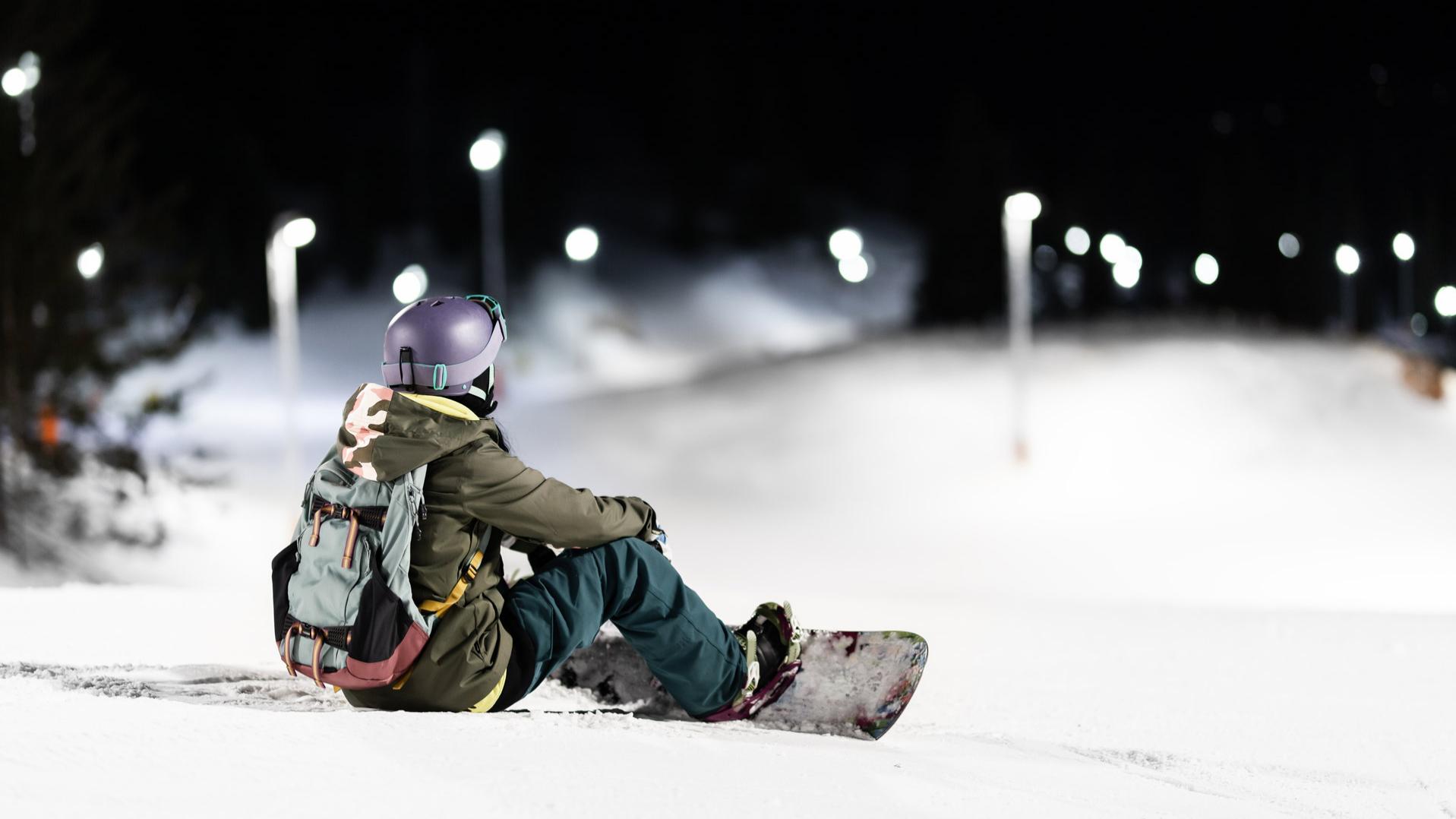 Image illustrating a person snowboarding at night on an illuminated ski slope