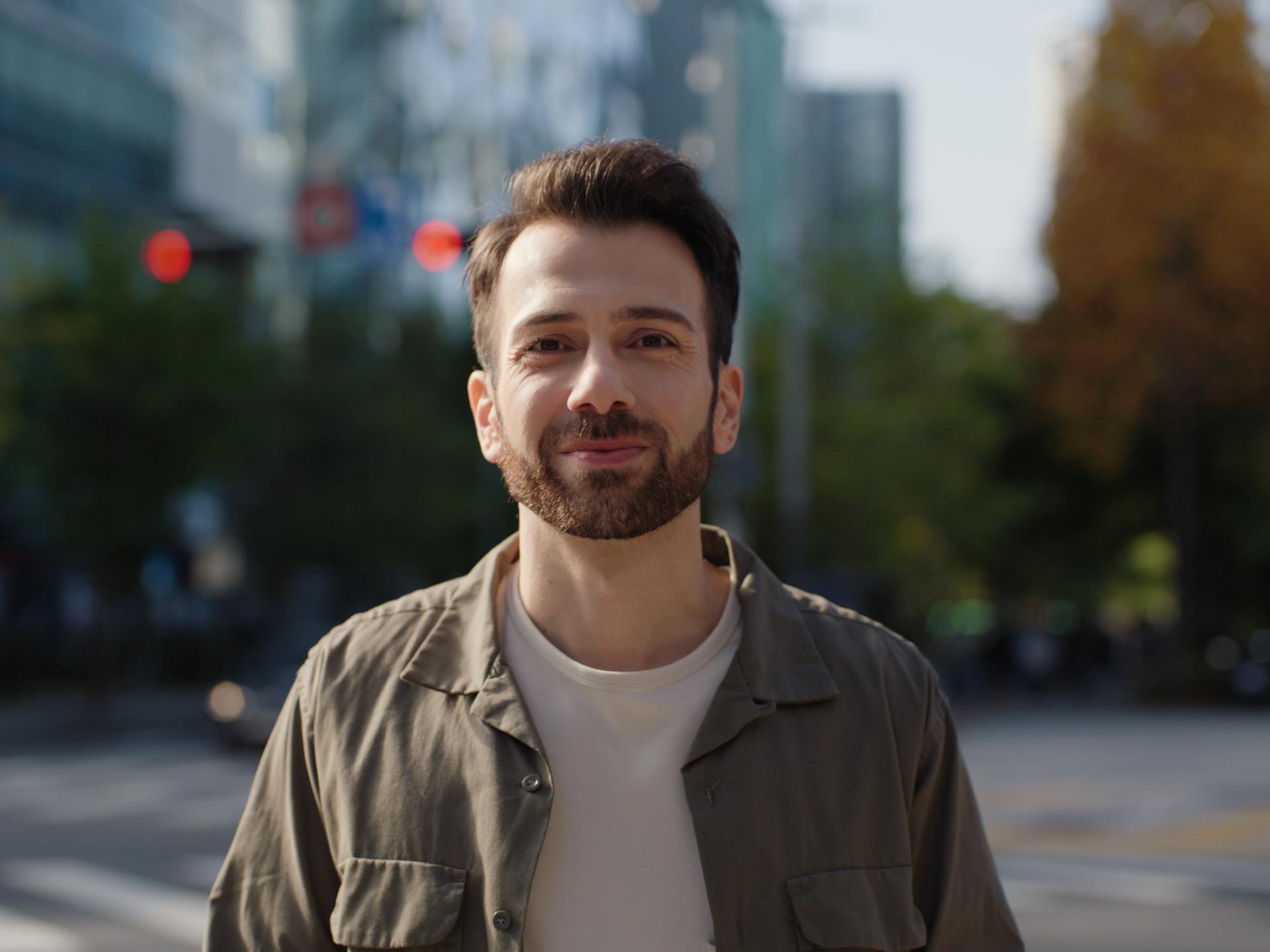 Bearded man smiling outdoors in a city environment, symbolizing confidence and visual freedom after LASIK treatment.