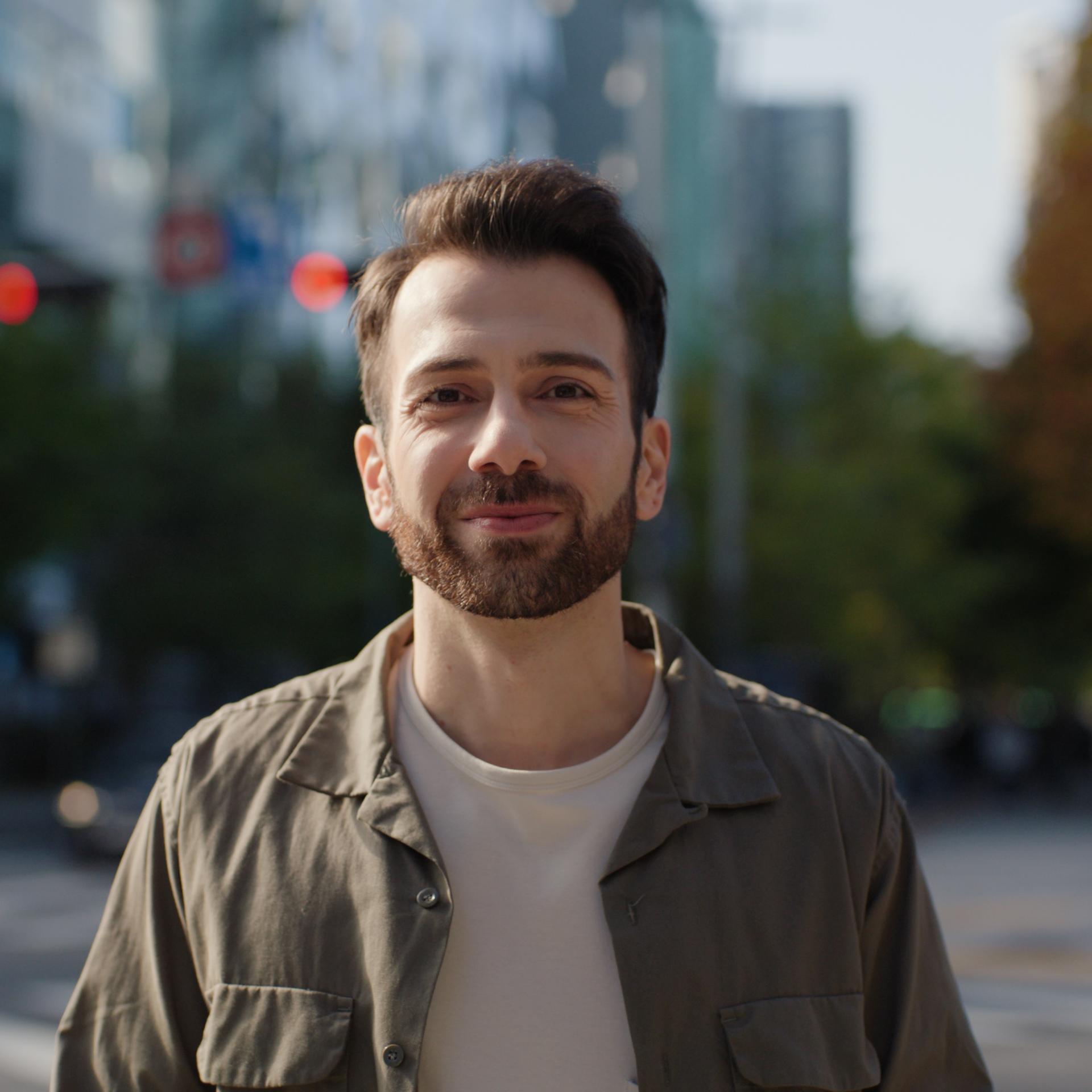 Bearded man smiling outdoors in a city environment, symbolizing confidence and visual freedom after LASIK treatment.