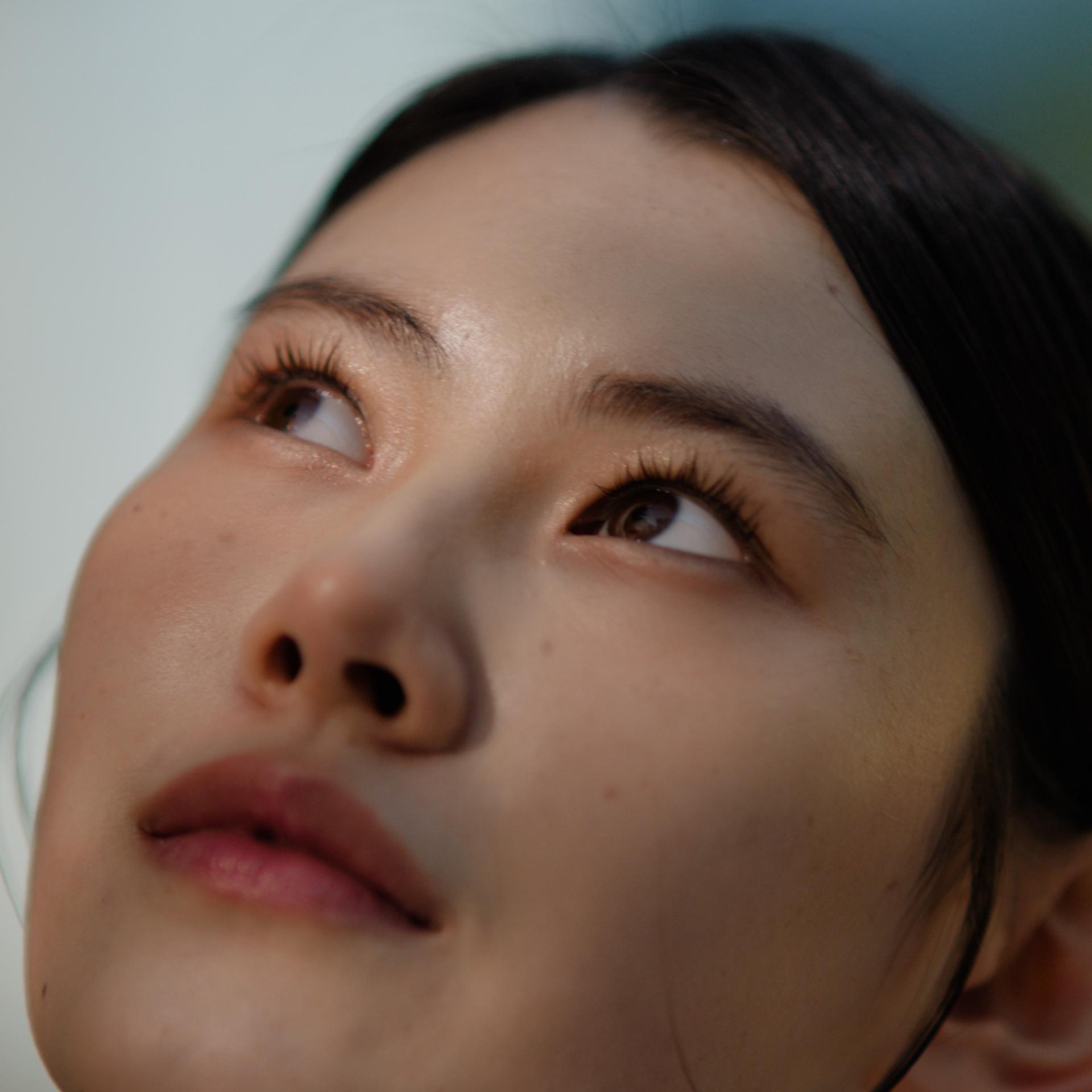 Close-up of a woman’s face looking upward thoughtfully, representing the healing period after LASIK eye surgery.