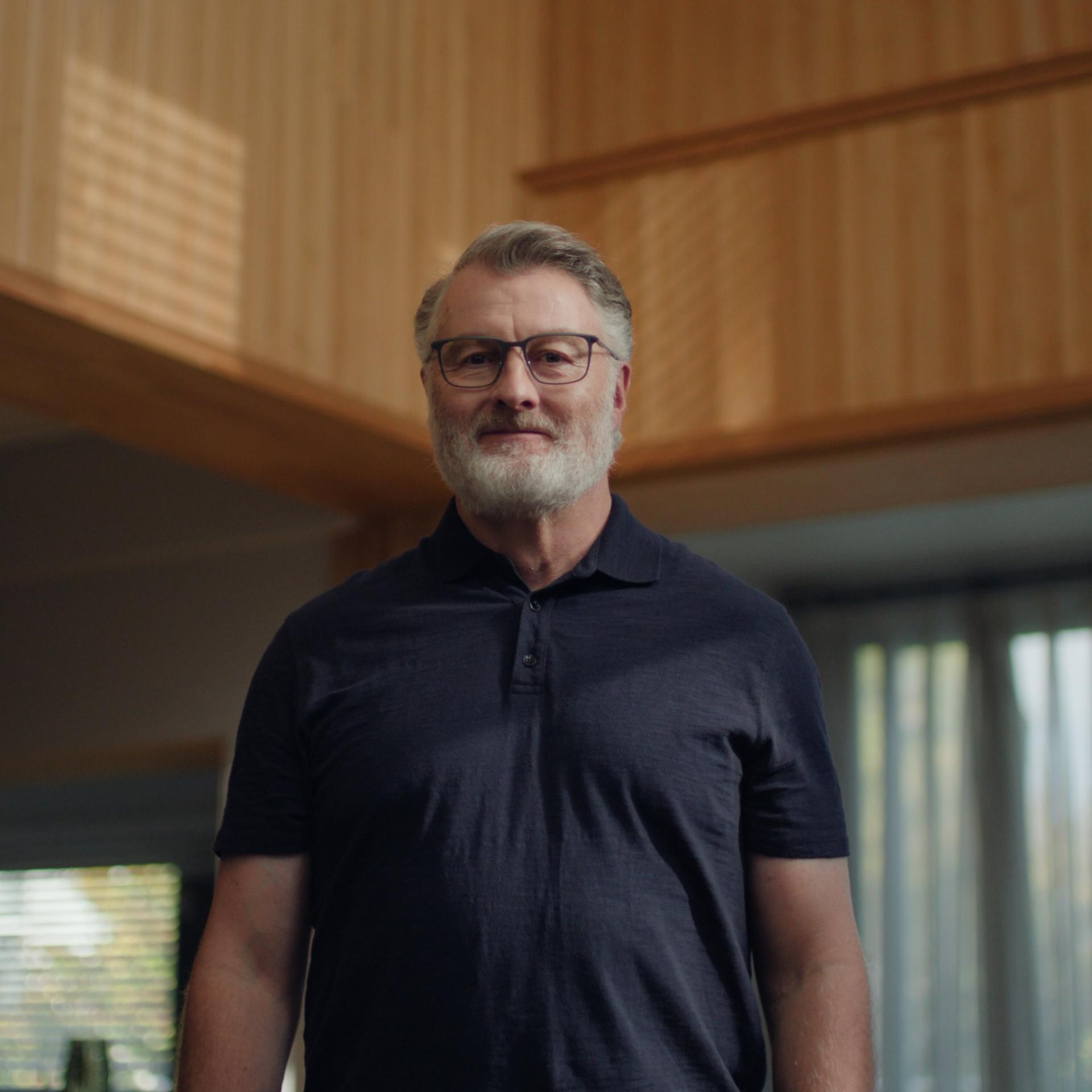 Older man standing in a sunlit living room wearing glasses, portraying a typical ZEISS PRESBYOND candidate with age-related vision concerns.