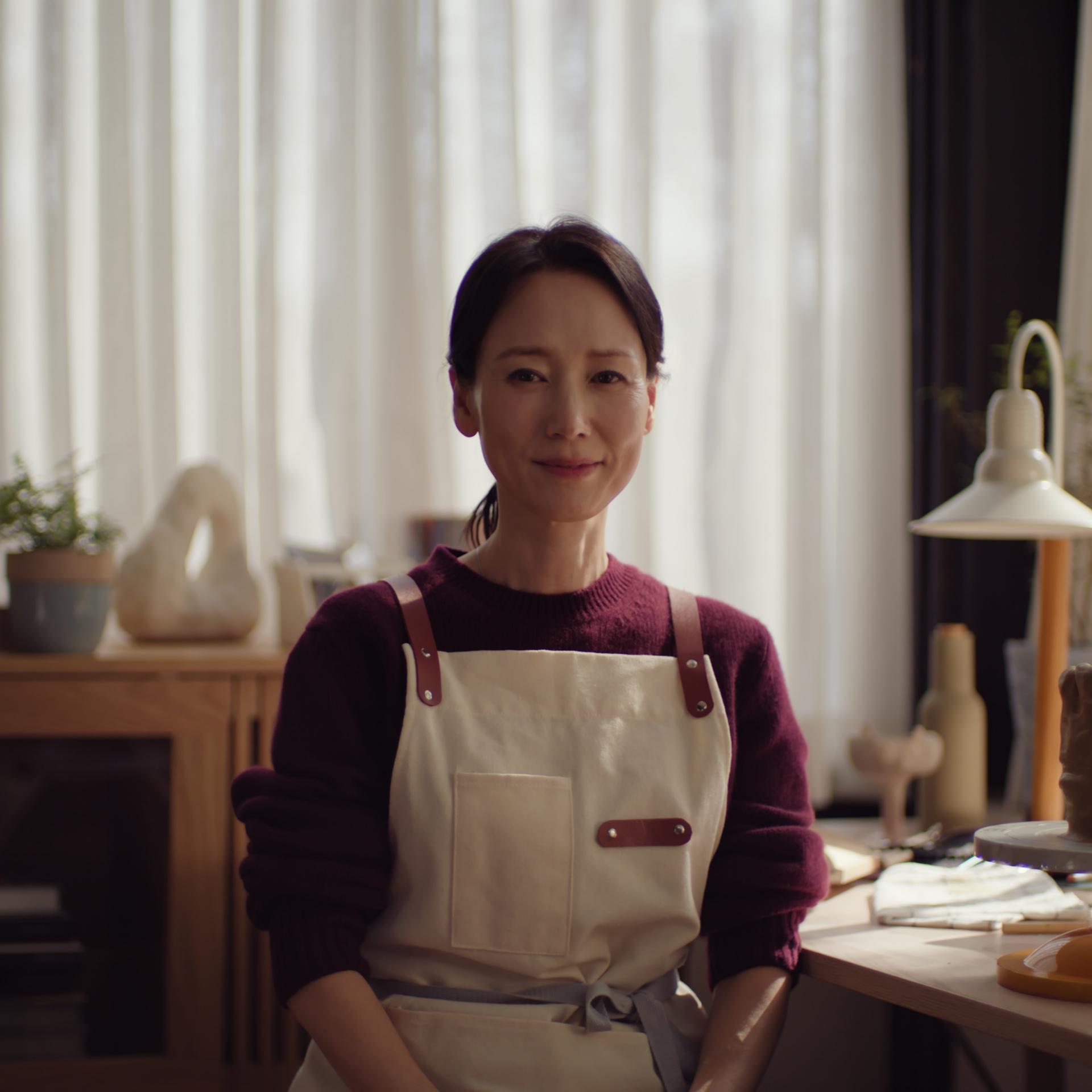 Middle-aged asian woman looking calmly into the camera wearing an apron.