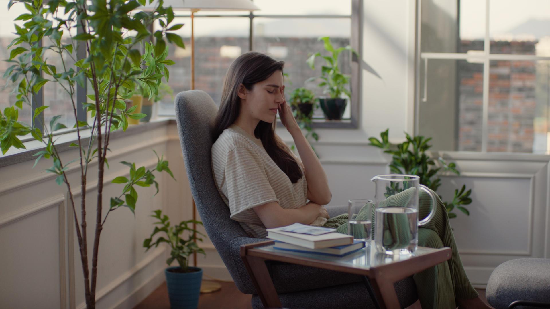 Woman resting in a chair, touching her face carefully—representing the importance of not rubbing the eyes post-surgery.