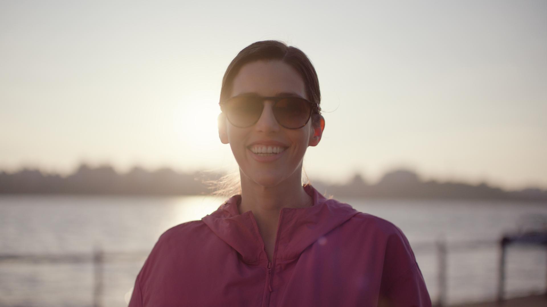Woman in sunglasses enjoying sunlight by the water after recovering from treatment with ZEISS SMILE pro.