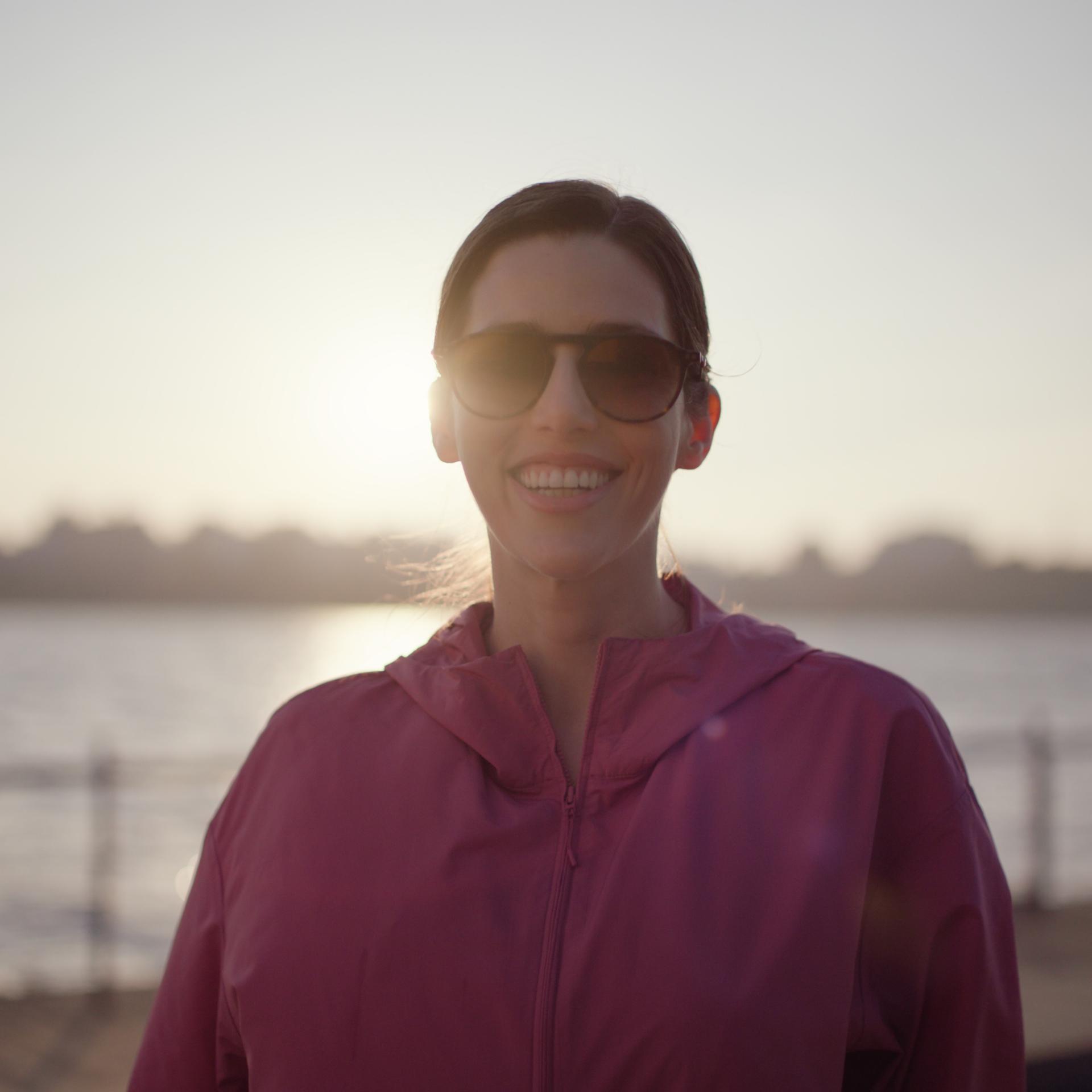 Woman in sunglasses enjoying sunlight by the water after recovering from lenticule extraction with ZEISS SMILE pro.