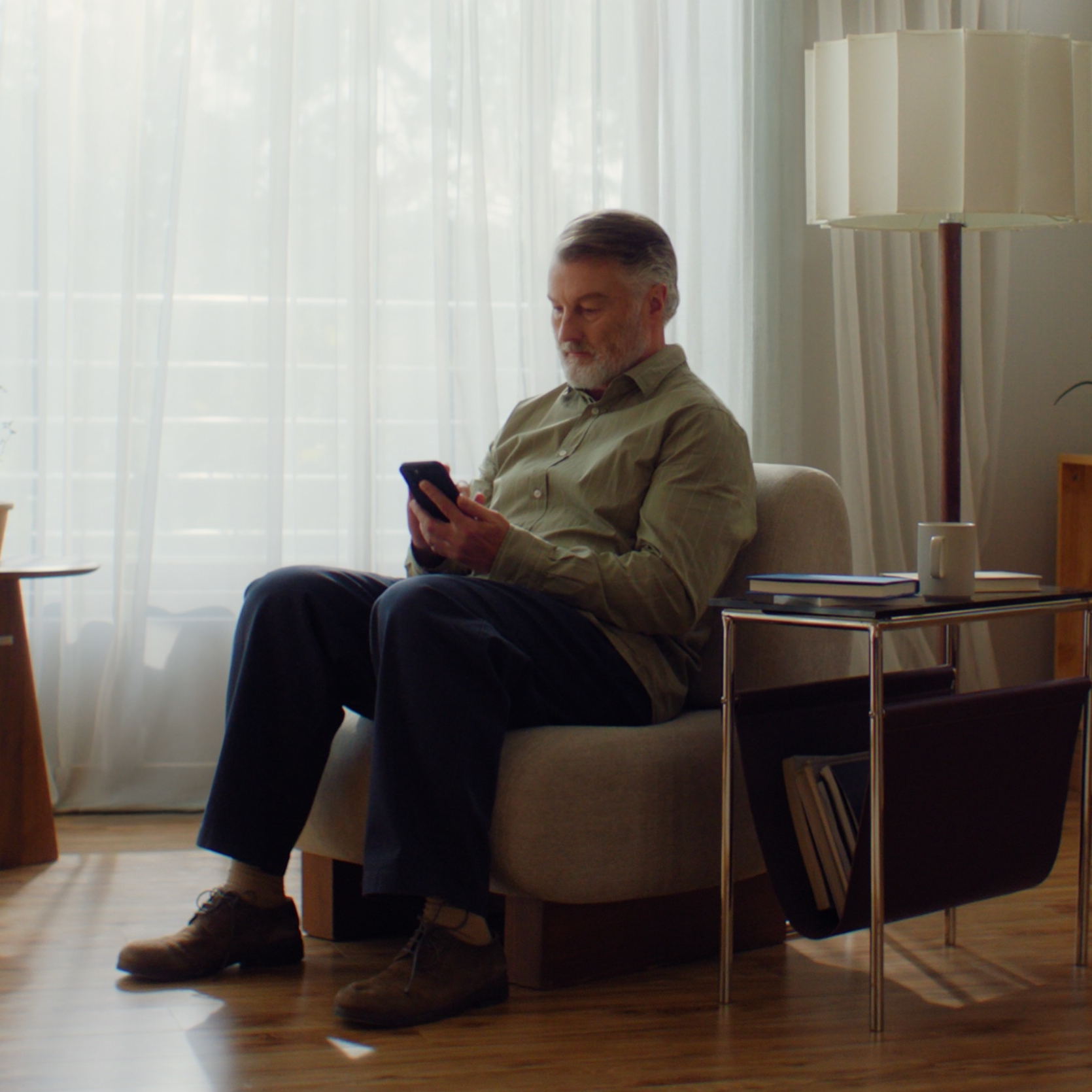 Older man using smartphone in a sunlit living room, representing clear near vision after treatment with ZEISS PRESBYOND.