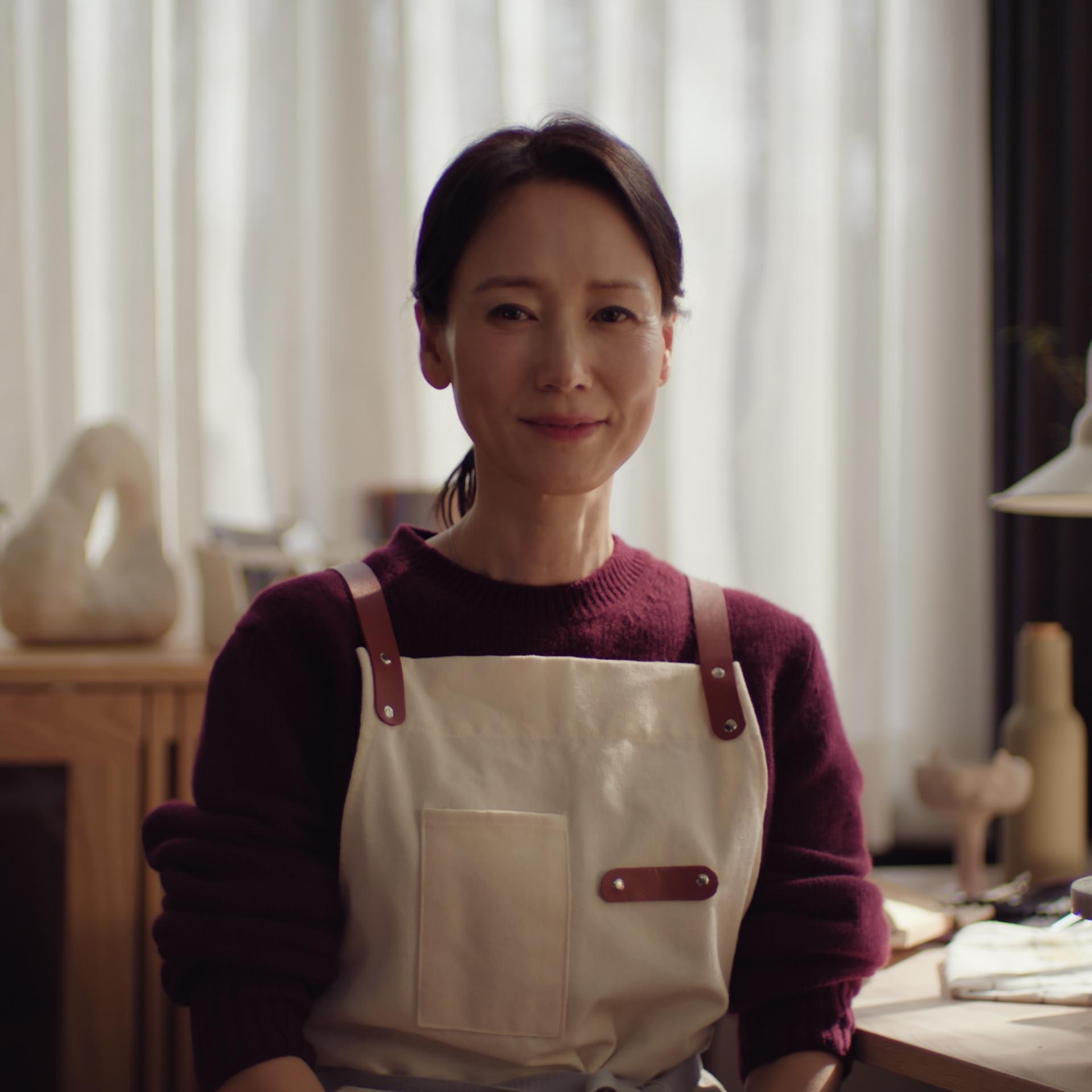 Middle-aged asian woman looking calmly into the camera wearing an apron.