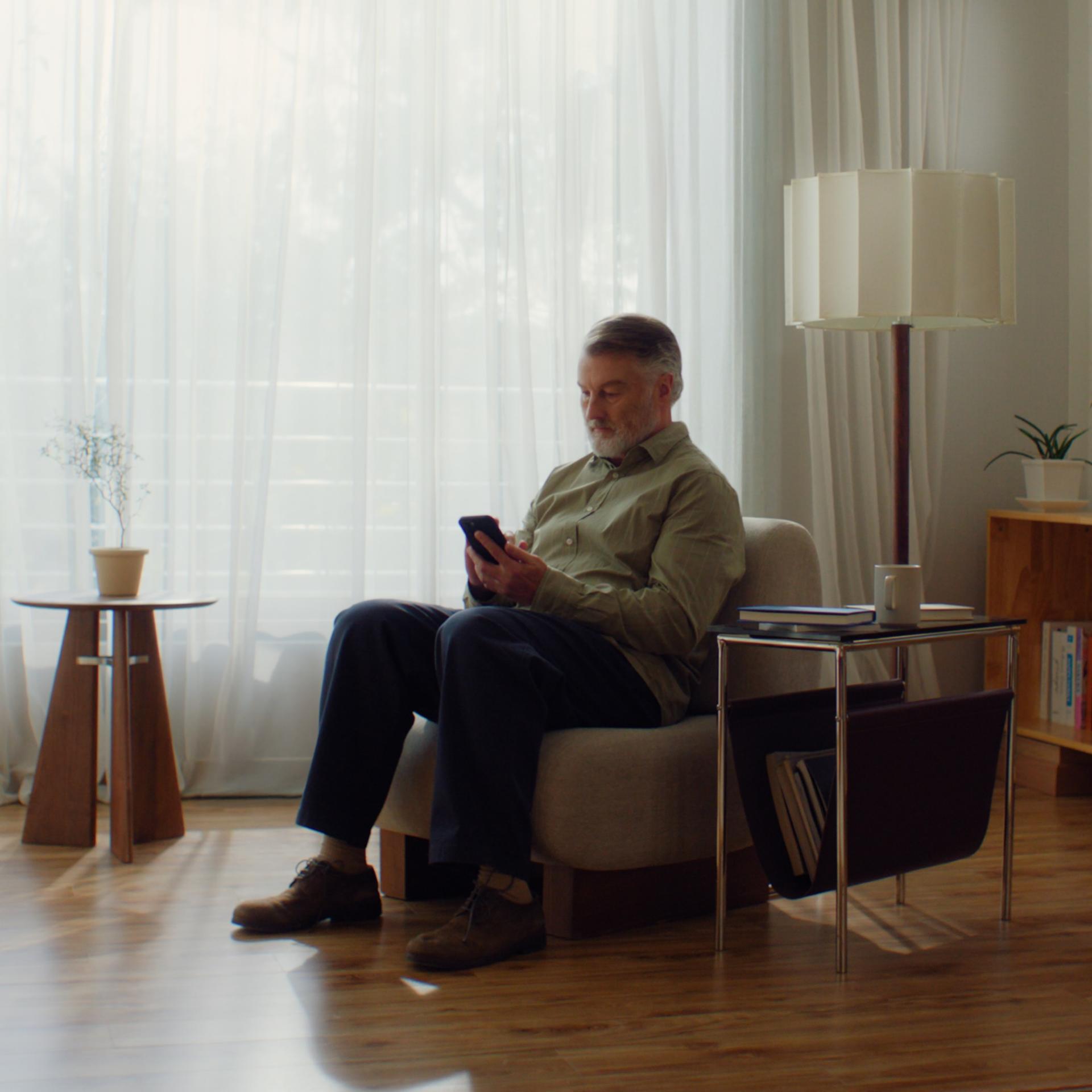 Middle-aged man sitting on a chair in a calm waiting room looking at his mobile phone.