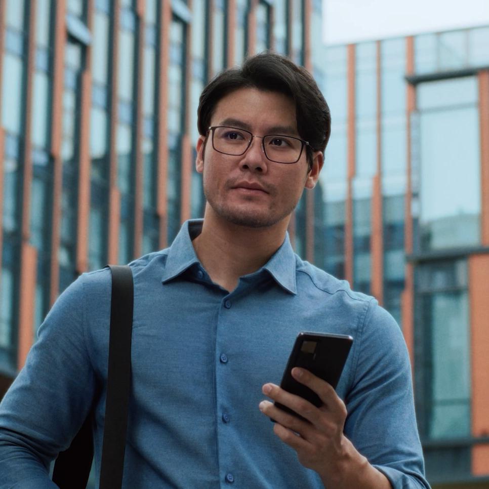 Man with glasses walking through city holding phone, symbolizing dependence on eyewear before undergoing PRK treatment.