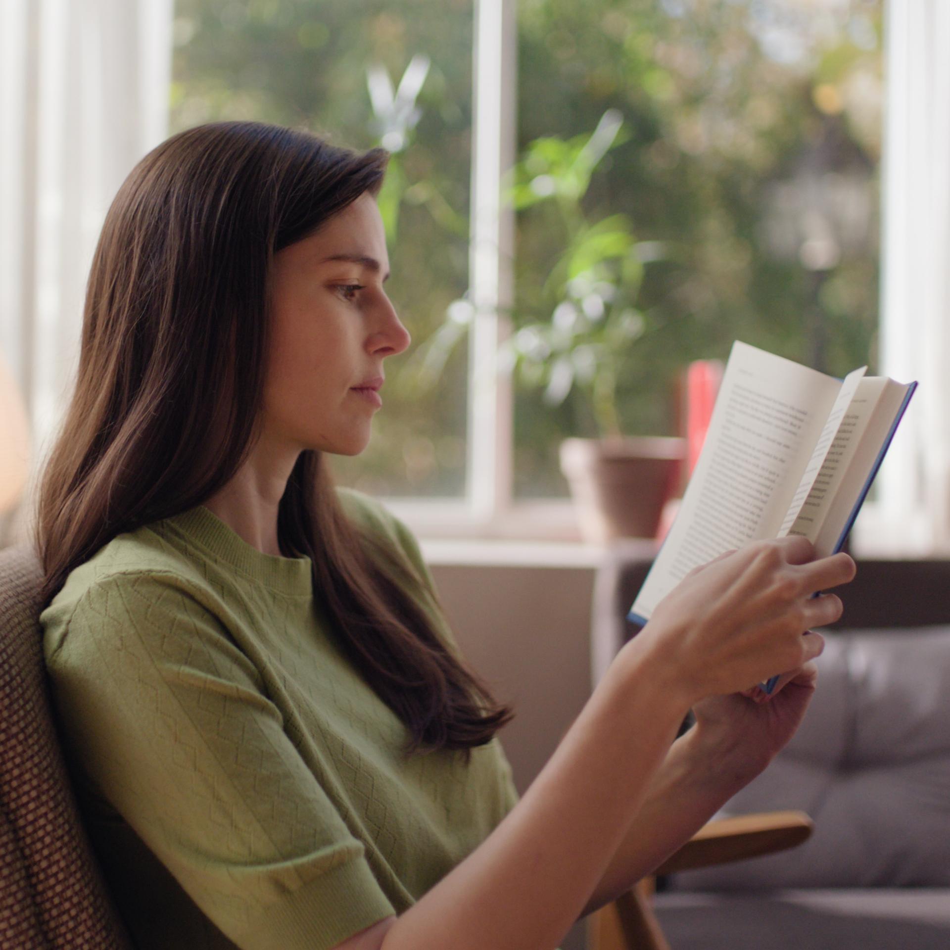 Woman reading comfortably in natural light, representing sharp, unaided vision after ZEISS SMILE pro treatment.