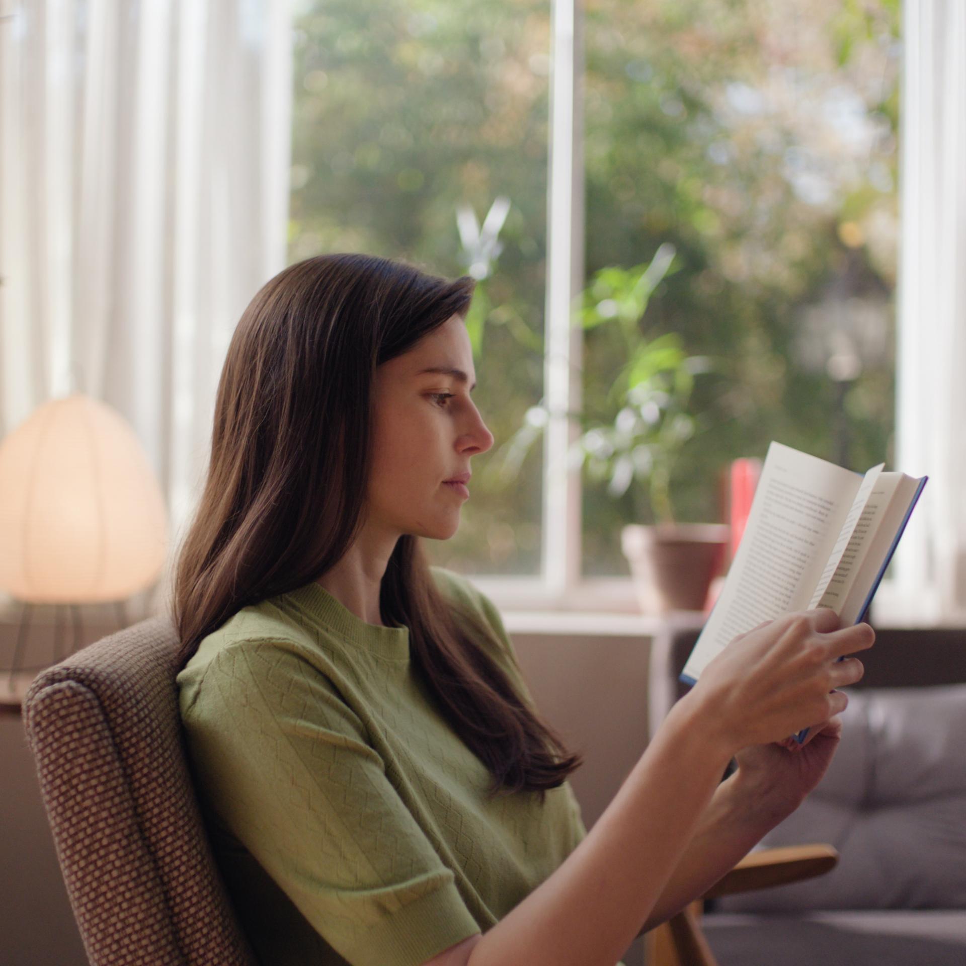 Woman reading comfortably in natural light, representing sharp, unaided vision after ZEISS SMILE pro treatment.