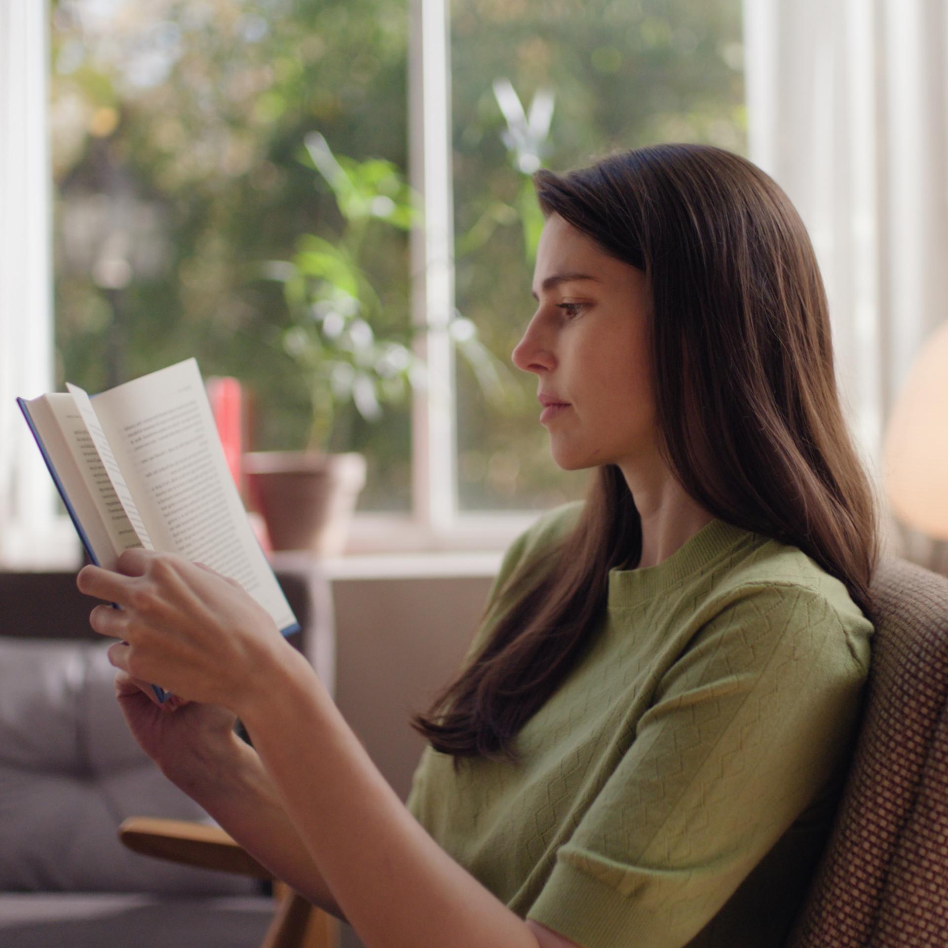 Woman reading comfortably in natural light, representing sharp, unaided vision after ZEISS SMILE pro treatment.