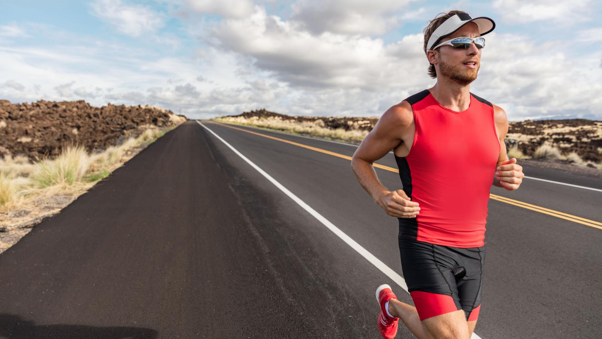 Runner fit athlete man running in triathlon suit training for Iron man on Hawaii. Fit male triathlete exercising endurance cardio on road.