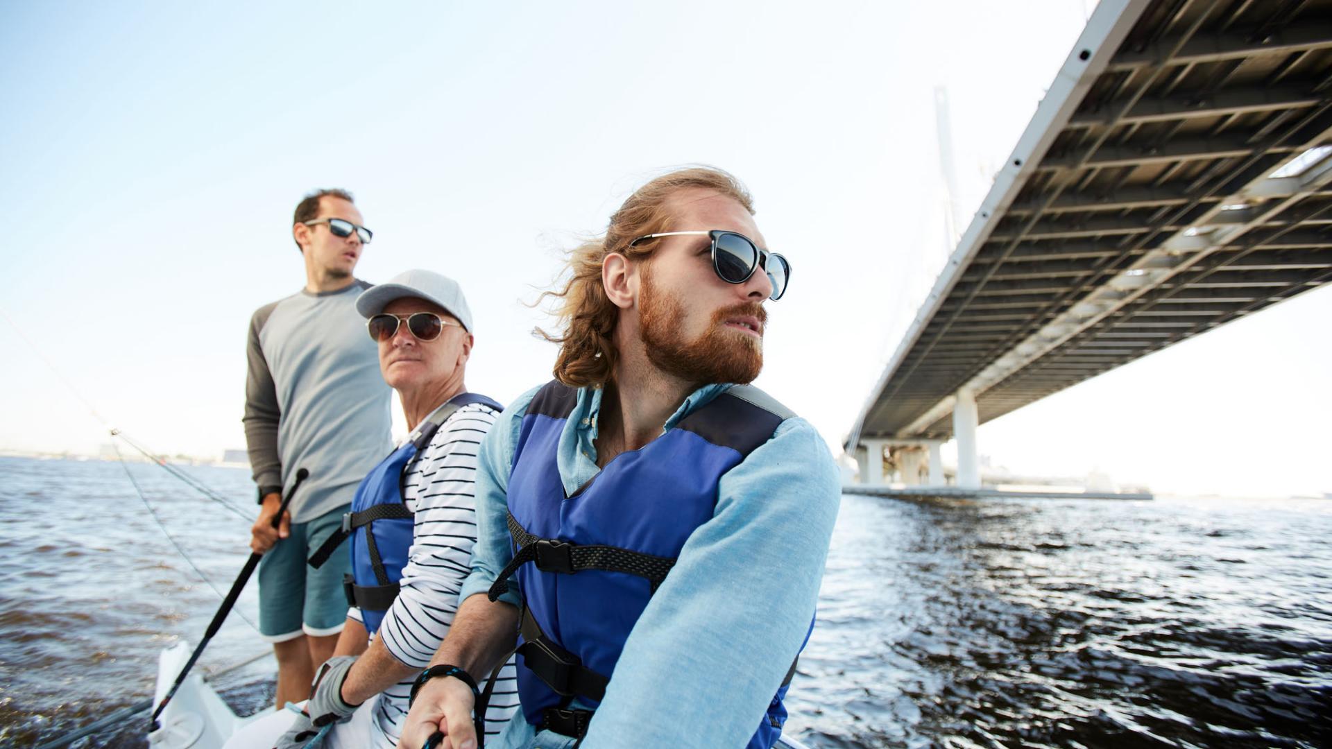 Pensive dreamy men of different ages sailing yacht together and enjoying floating on river, they looking around