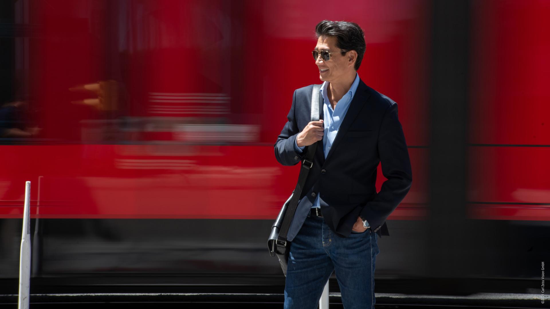 A person with sunglasses stands in front of a moving train.