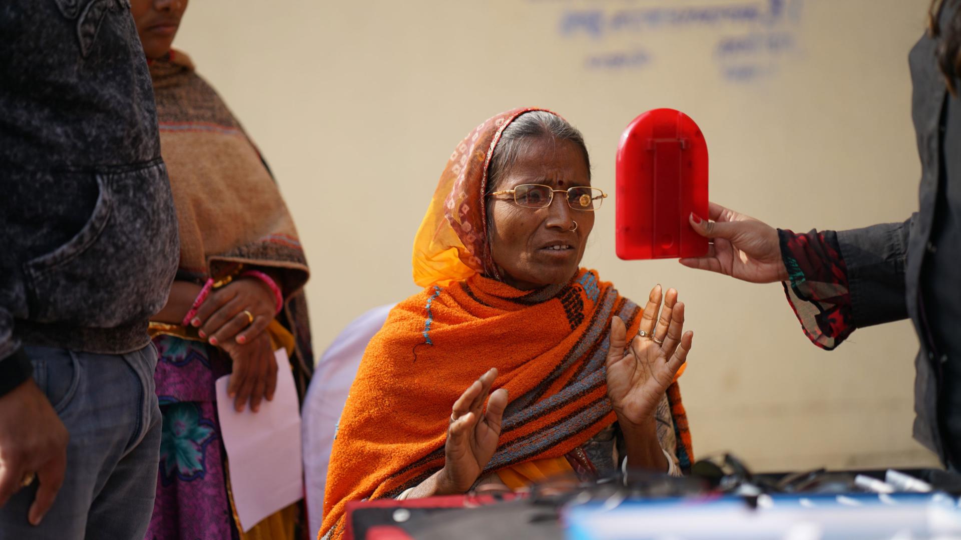 Indian woman with glasses looks into mirror.