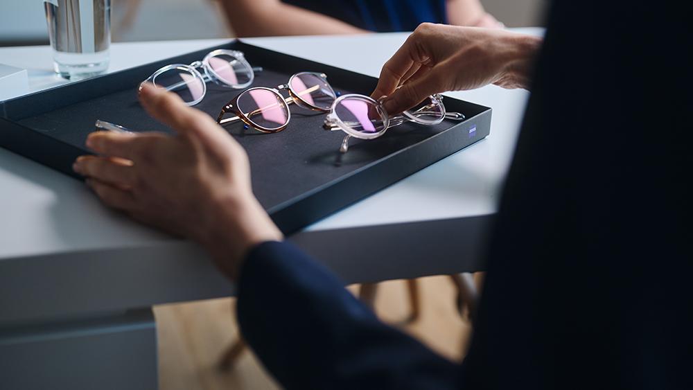 A hand picking a sample spectacle frame from a tray