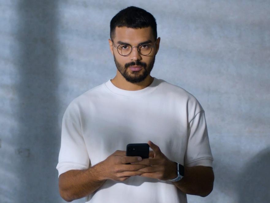 A young man wearing BlueGuard glasses, busy with his smartphone.