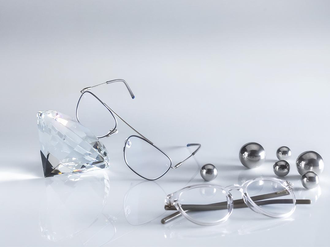 Two pairs of glasses with ZEISS lenses coated with the hardest and most hygienic DuraVision® AntiVirus Platinum coating. One pair of glasses leans against a crystal, the other lies flat on the floor next to silver. Both have clear lenses with no bluish reflection. 