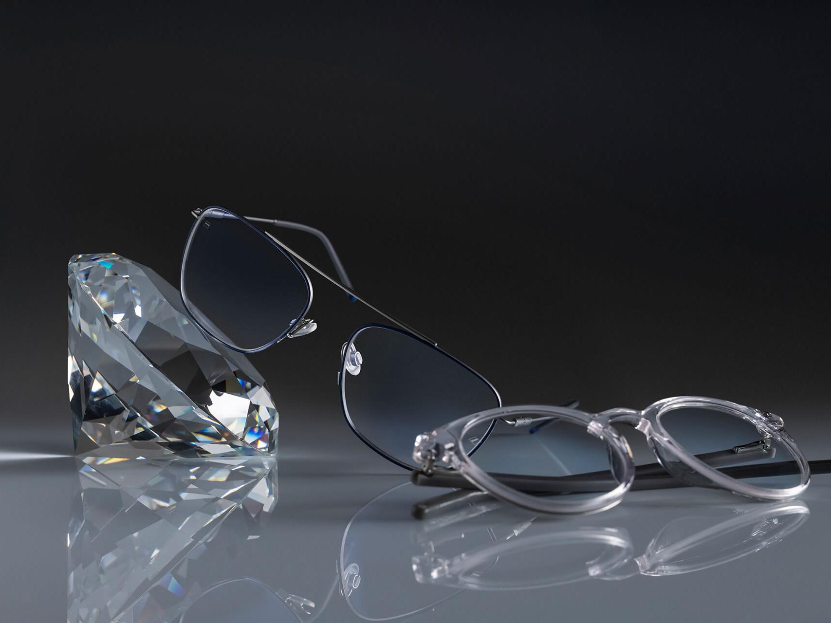 Two pairs of glasses with ZEISS lenses that have the hardest ZEISS coating ever – DuraVision® Platinum. One pair of glasses leans against a crystal, the other lies flat on the ground. Both feature clear lenses with no bluish reflection.