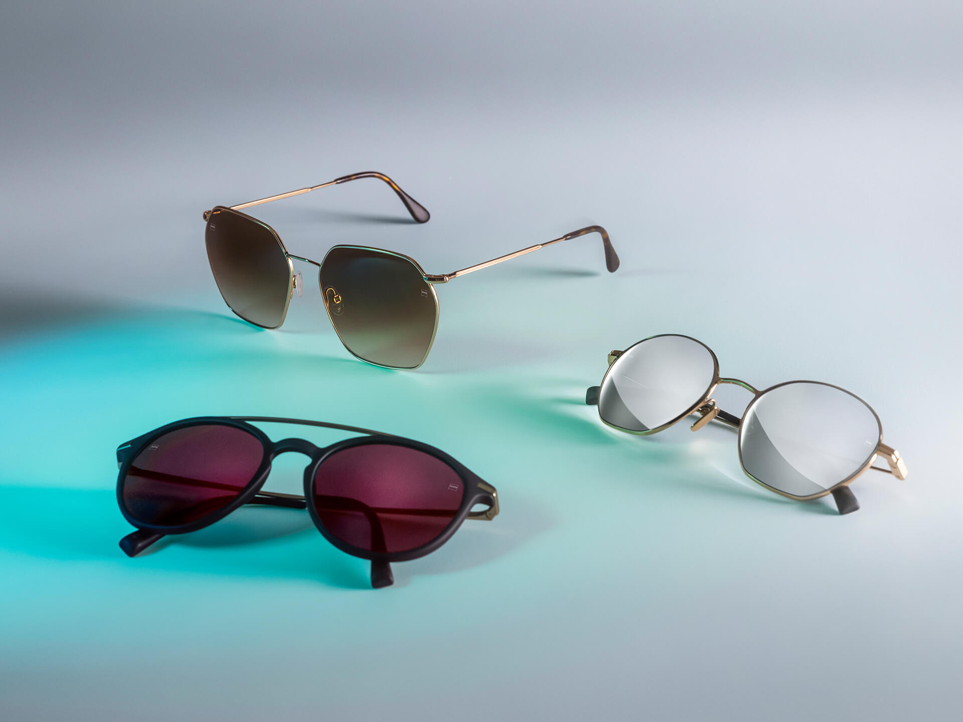 Three pairs of sunglasses with different colored ZEISS sunglass lenses, featuring DuraVision Sun, DuraVision Mirror and Flash Mirror coatings, visible on a white background with blue light reflection.