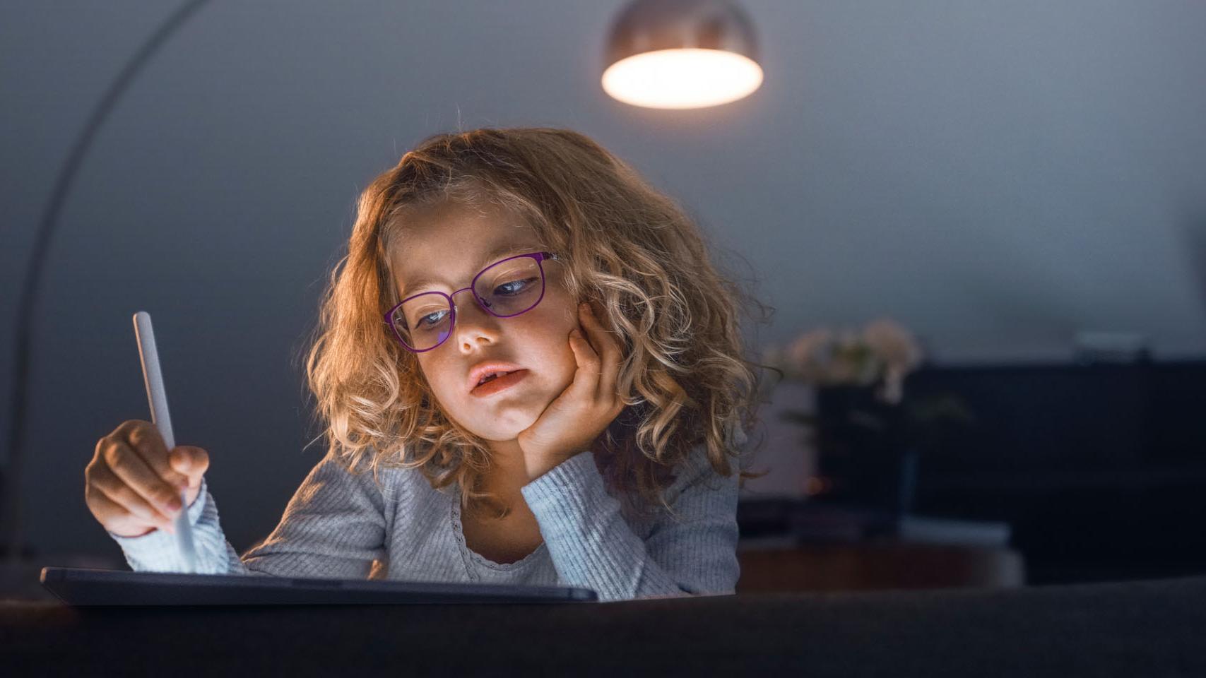 Little girl in a dark living room looking at a tablet.