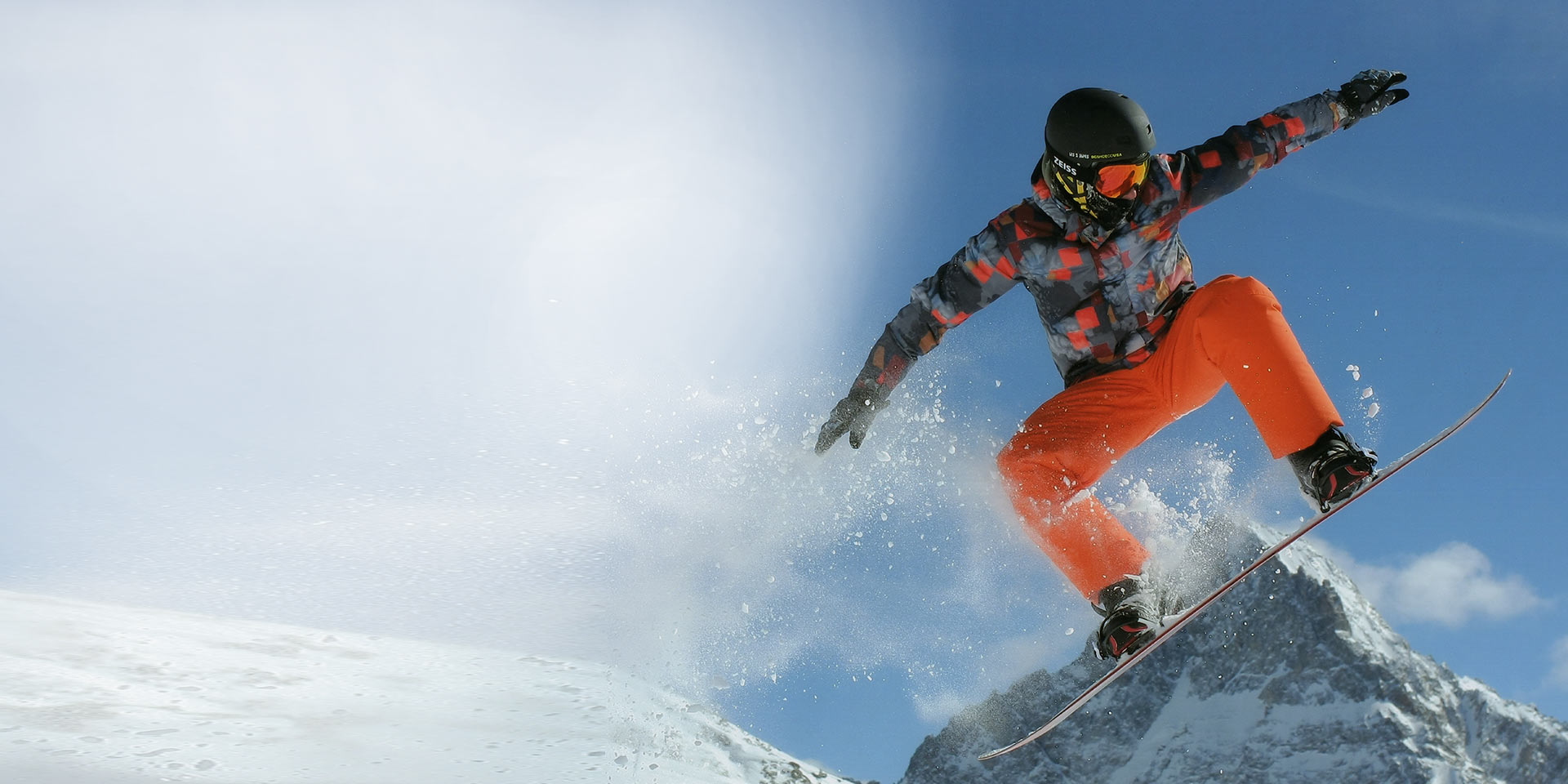 A man jumps with a snowboard, wears a black ski helmet and ZEISS snow goggles with Interchargeable technology for protection