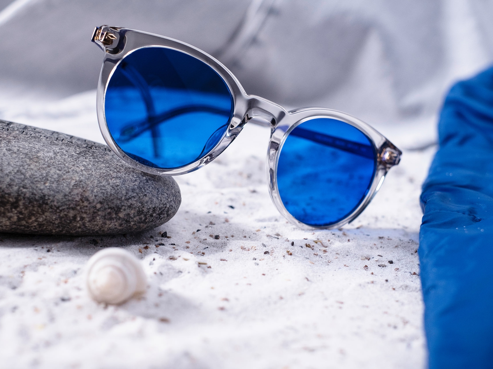 Изображение солнцезащитных очков с синей тонировкой, наполовину лежащих на камне