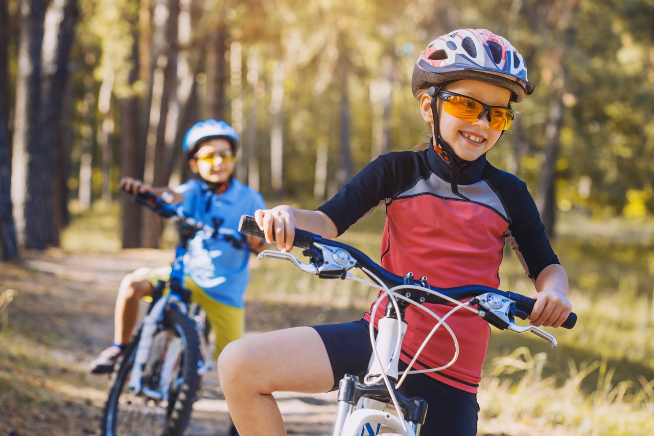 Kids on bicycles in the sunny forest. Children cycling outdoors in helmet