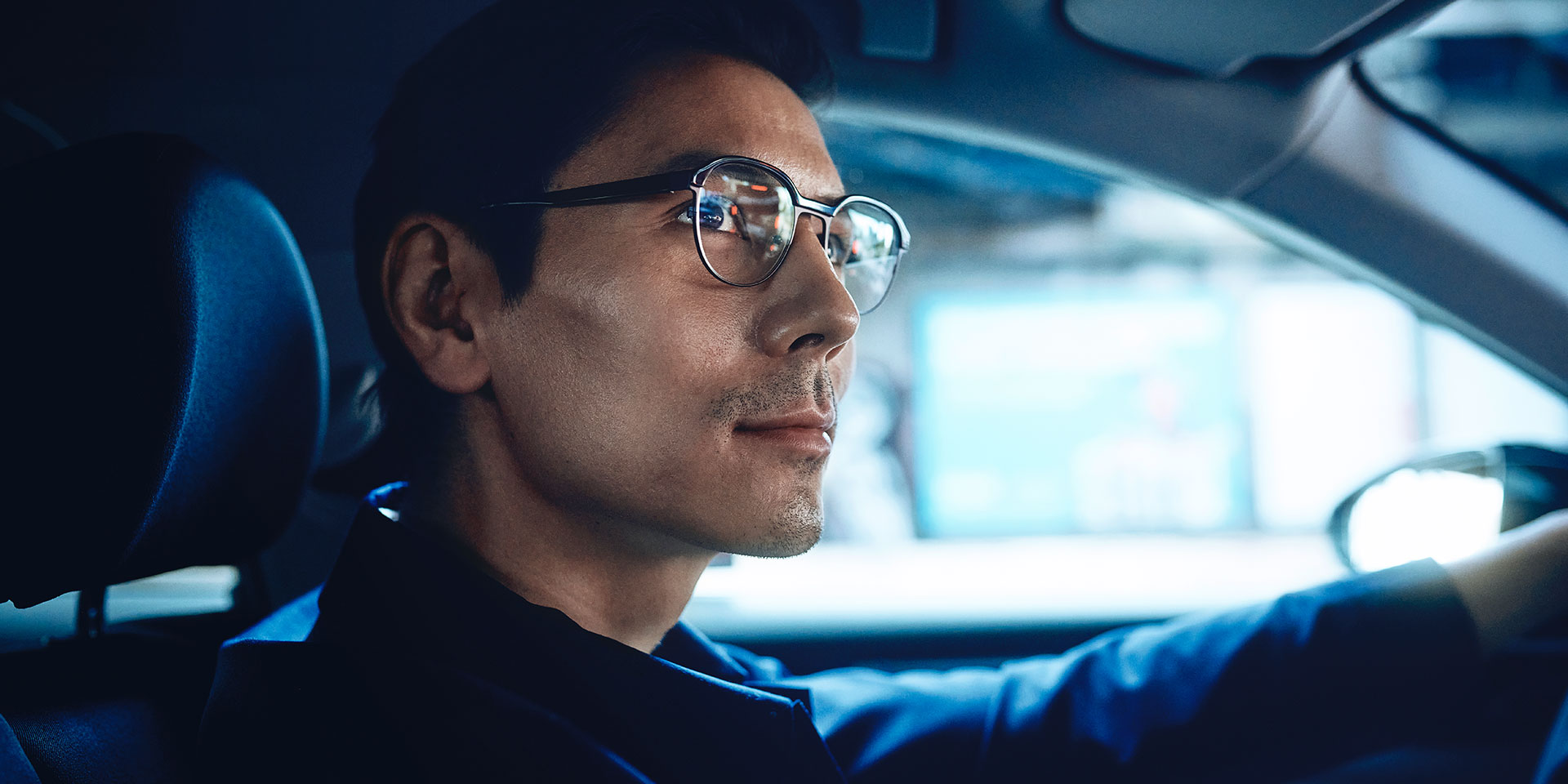 Man driving a car, looking self-confident with a slight smile on the road. He is wearing ZEISS Single Vision DriveSafe lenses.