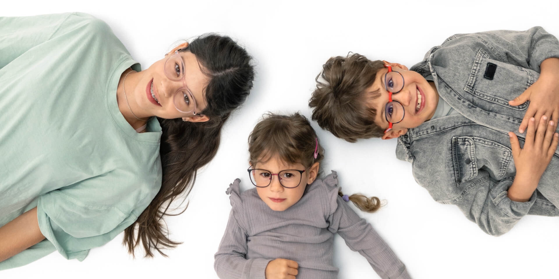 A teenager and two younger children lie on the floor wearing ZEISS Myopia lenses.