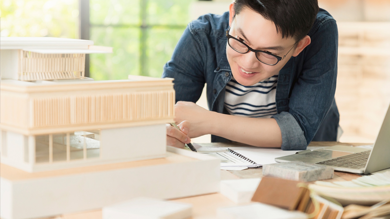 Middle aged man with short black hair wearing ZEISS Office glasses to help him focus on the details of an intricate architectural model. 