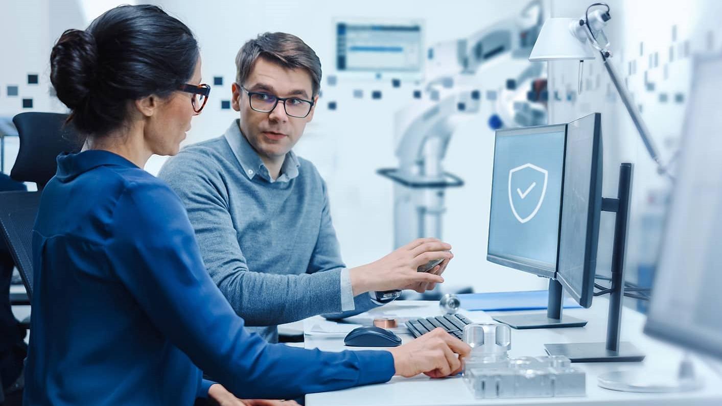 Two professionals are discussing work at a computer workstation in a high-tech laboratory environment.