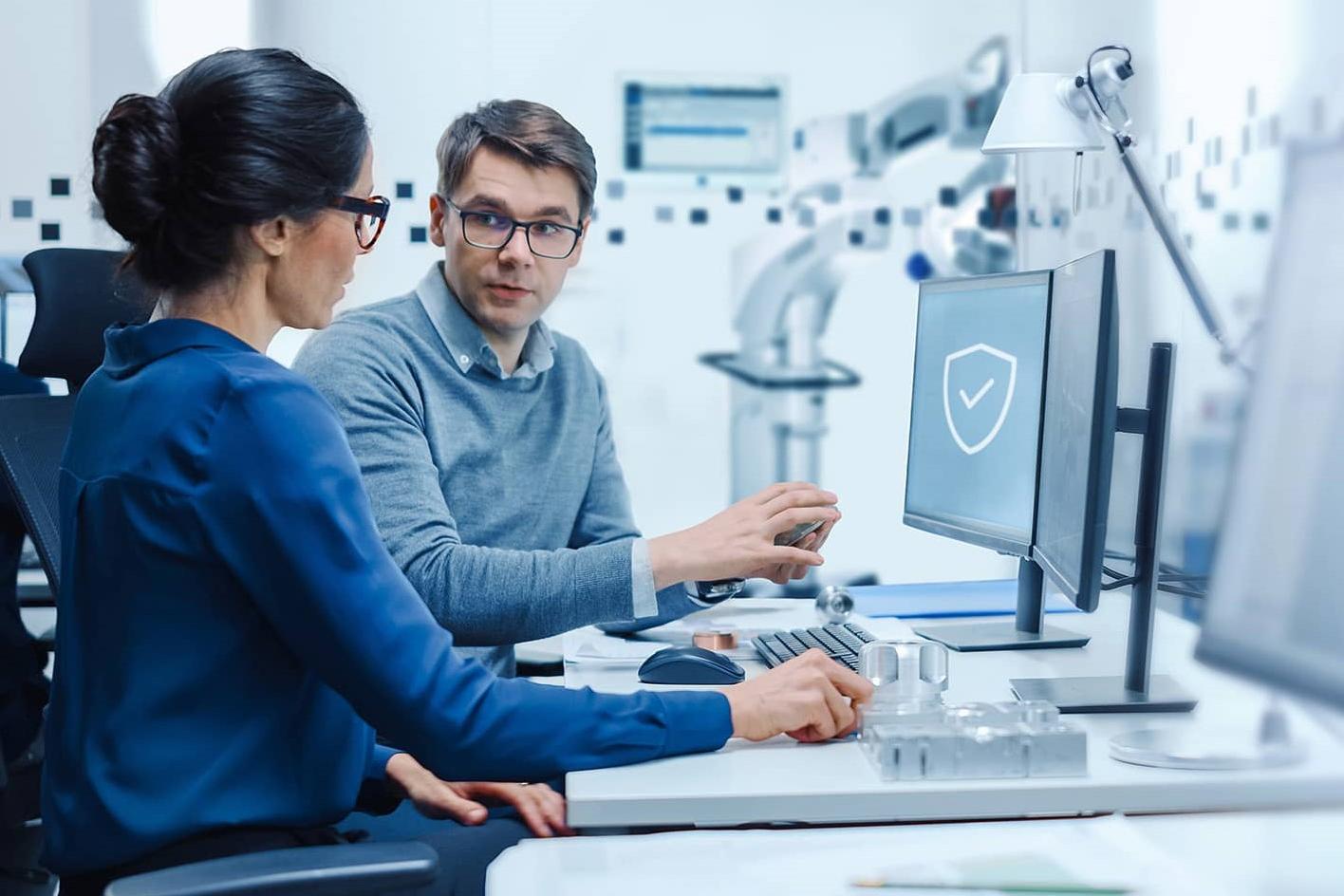 Two professionals are discussing work at a computer workstation in a high-tech laboratory environment.