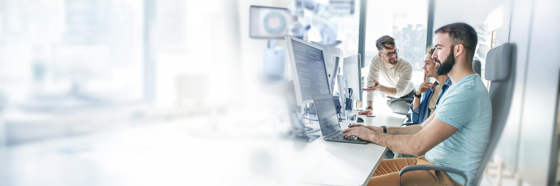 A team of three working focussed on desktop computers.