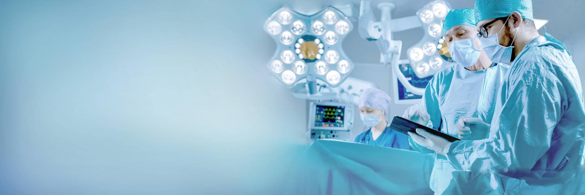 Surgeons in an operating room environment are reviewing information on a tablet under bright surgical lights, with ZEISS medical equipment visible.