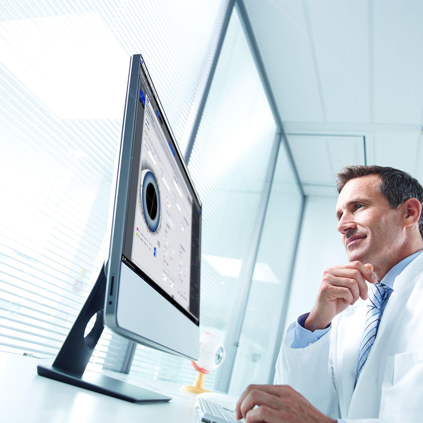 Man in lab coat looks at screen showing eye measurement software. 