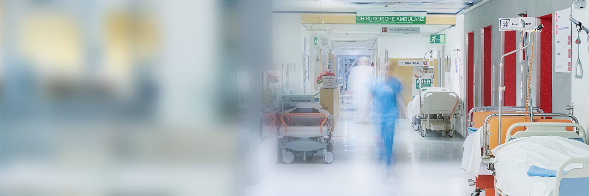 A hospital corridor with medical beds, equipment, and a blurred figure of a healthcare professional walking.